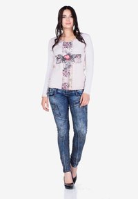 Hellrosa Langarmhemd mit floralem Muster und Herzdesign, kombiniert mit blauen, lässig geschnittenen Slim-Fit-Jeans und schwarzen High Heels.