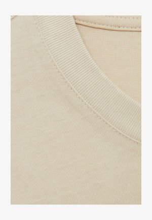 Beež puuvillane T-särk, millel on soonikkselg ja sile tekstuur. Õmblusdetail kaeluse ääres lisab peene aktsendi.
