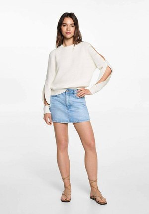 Ljust beige ribbat tröja med öppna ärmskärningar, i kombination med en ljusblå denim minikjol, och tanfärgade sandaler med remmar.