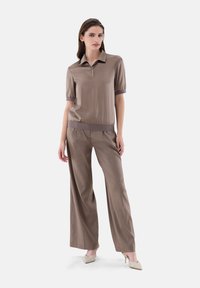 Braunes Polohemd mit kurzen Ärmeln, Kragen und elastischem Saum, kombiniert mit weit geschnittenen Hosen aus dem gleichen Material und in der gleichen Farbe, schafft einen einheitlichen Look.
