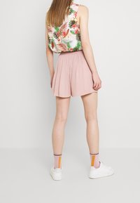 Shorts plisados de color rosa claro con cintura elástica, combinados con un top sin mangas con estampado floral y detalles en verde y rojo.