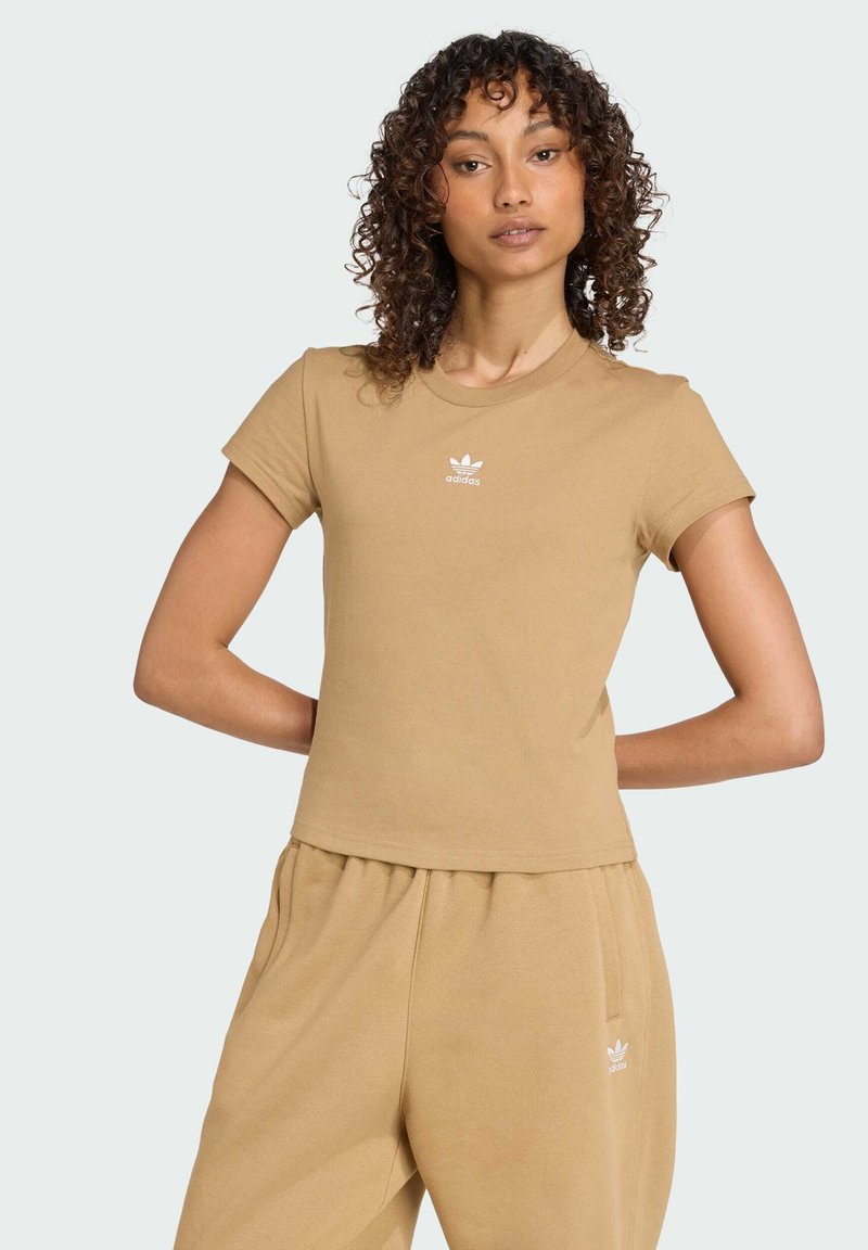 Camiseta ajustada color marrón claro hecha de algodón, con mangas cortas y cuello redondo; presenta un pequeño logo blanco de Adidas en el pecho.
