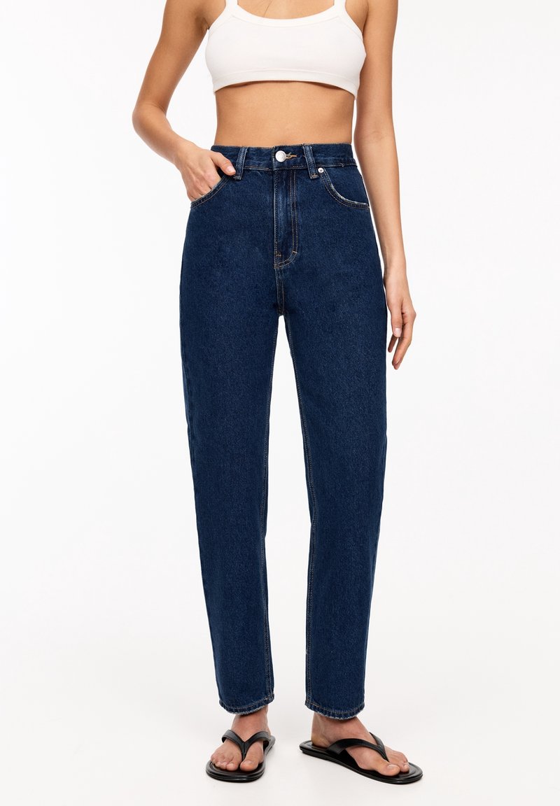 Jean en denim bleu foncé taille haute avec une coupe droite, des coutures contrastantes et un agencement classique à cinq poches.