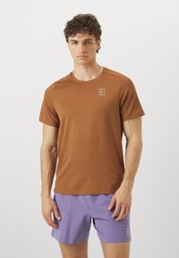 T-shirt castanho de mangas curtas com gola redonda e pequeno logótipo branco. O tecido é suave e o design é ajustado com uma silhueta equilibrada.