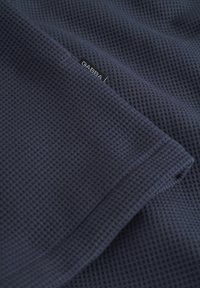 Tela texturizada de color azul marino con un patrón de gofre, que presenta una pequeña etiqueta negra "GABBA" en el borde, mostrando un diseño suave y transpirable.