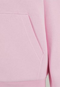 Sudadera de color rosa claro con bolsillo tipo canguro, puños acanalados y una textura suave con detalles de costuras visibles.