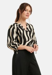 Black and white striped blouse in lightweight fabric, featuring a V-neck and elastic cuffs with ties, paired with black pants.
