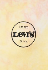Levi's-logo geborduurd in zwarte draad binnen een cirkel op geel en roze tie-dye stof, met de tekst "EST. 1873" en "SF / CA."
