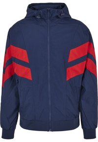 Veste à capuche bleu marine avec fermeture éclair intégrale et bandes chevrons rouges sur le haut des manches et la poitrine, poignets élastiques et ourlet à la taille.