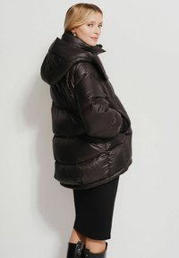Czarna puchowa kurtka o błyszczącym wykończeniu, z oversize'owym kapturem i elastycznymi mankietami. Posiada pikowany fason oraz boczne kieszenie, które zapewniają dodatkowe ciepło.