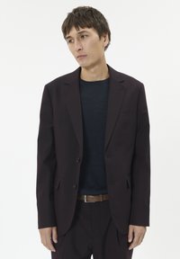 Blazer maroon adaptat, cu două butoane, rever clasic și buzunare laterale, asortat cu o cămașă albastră închisă și o curea maro. Textură de stofă netedă.