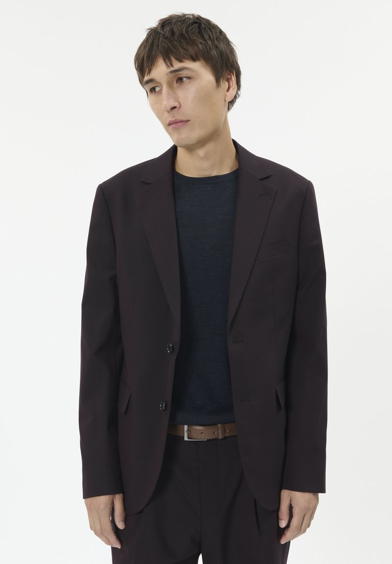 Blazer maroon adaptat, cu două butoane, rever clasic și buzunare laterale, asortat cu o cămașă albastră închisă și o curea maro. Textură de stofă netedă.