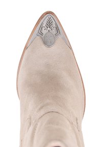 Botín de ante beige hasta el tobillo con punta afilada, que presenta un acento metálico plateado en la punta y detalles en relieve en el herraje.