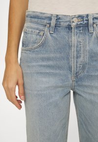 Ljusblå denimjeans har en medelhög midja, femficksdesign och subtila whiskeringar längs låren. Klassisk knapplåsning och dragkedja.