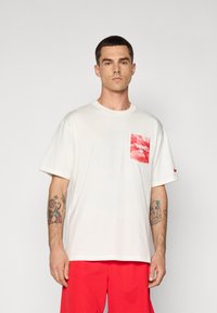 Hvid bomulds T-shirt med en stor rød grafisk lomme, der har et okse-design, korte ærmer og ribbet rund hals.