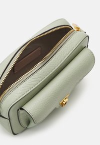 Miętowozielona skórzana torba o teksturowanym wykończeniu, złotym suwak i brązowym wnętrzu. Posiada przednią kieszeń do dodatkowego przechowywania.