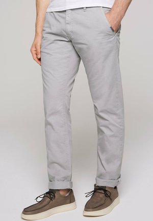 Chinos en coton gris clair avec une coupe droite, des ourlets retroussés, des poches latérales et une texture subtile, associés à des chaussures marron.