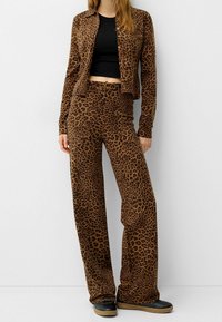 Hnědý kardigan s leopardím potiskem a odpovídající široké kalhoty z měkké tkaniny. Outfit má zkrácený střih a ploché černé boty.