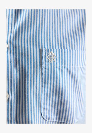 Siniste ja valgete vertikaalsete triipudega särk, millel on rinnal tasku ning tasku kohal valgete tikitud initsiaalidega.