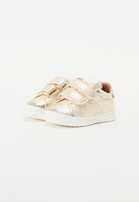Złote metaliczne sneakersy dla przedszkolaków z podwójnymi zapięciami na rzep, białą gumową podeszwą, zaokrąglonym noskiem i delikatnym różowym akcentem na pięcie.