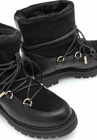 Czarne botki za kostkę z zamszową cholewką, podszyciem z futra sztucznego, metalowymi ozdobami oraz teksturowaną gumową podeszwą o wytrzymałym bieżniku.