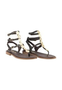 Sandalias planas negras con acentos circulares dorados, que presentan múltiples correas y un diseño tipo tanga. Suela suave con un tacón marrón claro.