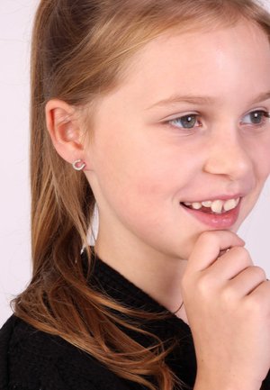 Silberne Ohrstecker in Herzform mit einer glatten Metallic-Oberfläche. Ein Kind mit langen, hellbraunen Haaren und einem schwarzen Kleidungsstück wird gezeigt.