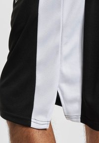 Shorts de sport noir et blanc avec une texture en maille, présentant une bande blanche en biais. Comprend une fente sur le côté pour améliorer la mobilité.