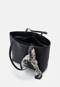 Bolso tote de cuero negro con asas largas, con una parte superior abierta y un bolsillo interior, adornado con una bufanda de seda estampada con flores.