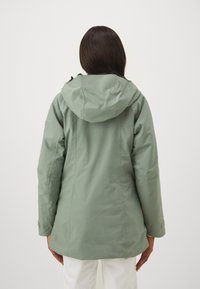Vattentålig grön ytterjacka med huva. Har en ren design, jämn yta och justerbara ärmslut.