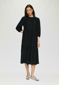 Schwarzes Midi-Kleid mit Dreiviertelärmeln, gepufftem Ausschnitt, gestuftem Design, aus leichtem Stoff, kombiniert mit silbernen Ballerinas.