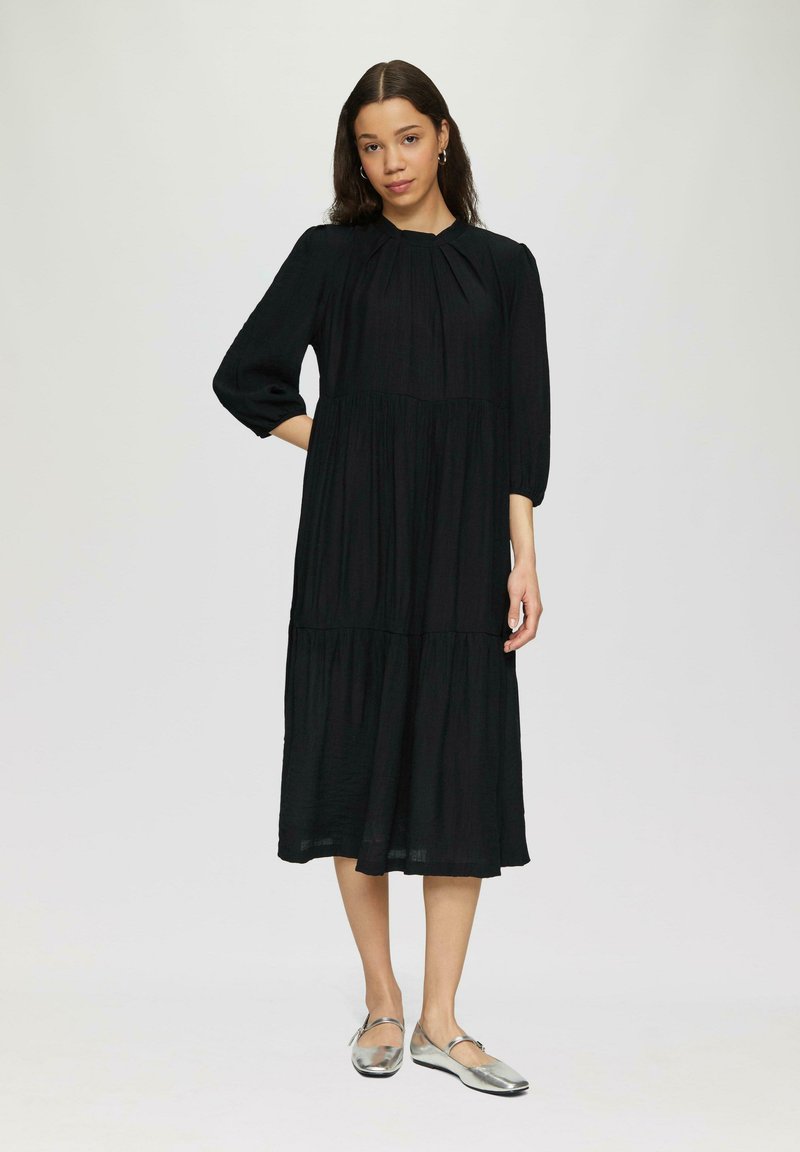 Schwarzes Midi-Kleid mit Dreiviertelärmeln, gepufftem Ausschnitt, gestuftem Design, aus leichtem Stoff, kombiniert mit silbernen Ballerinas.