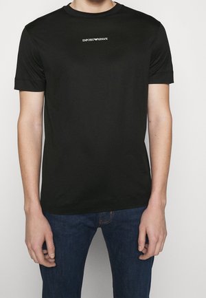 Czarna koszulka z krótkim rękawem, wykonana z gładkiego materiału, z okrągłym dekoltem i białym logo "Emporio Armani" na klacie. Prosty design.