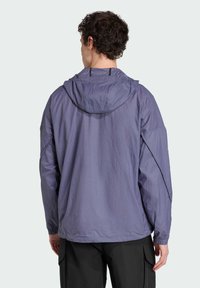 Lightweight, purple, hooded jacket with a textured exterior and elastic cuffs, worn over black cargo pants.