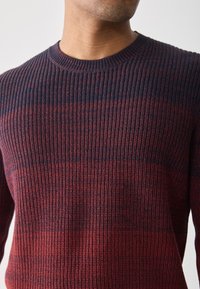 Pulover tricotat cu dungi roșii și bleumarin, cu guler rotund, având textură ribbed și un design ajustat.