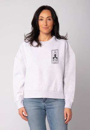 Sweatshirt gris clair avec une coupe décontractée, mettant en avant un imprimé graphique sur la poitrine gauche représentant un lion et une silhouette, ainsi que des poignets côtelés.
