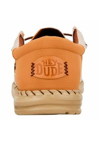 Scarpa slip-on arancione in tela con suola in tessuto color nocciola. Presenta una toppa con logo cucita sul tallone e dettagli marroni.