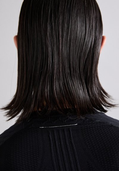 Peça de vestuário de malha preta com padrões texturizados, apresentando detalhes em canelado e uma costura traseira. Cabelo liso e direito caindo logo abaixo dos ombros.