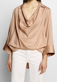 Beige, satiiniblouse, jossa on laskostettu pääntie, taitettavat hihansuut ja rento istuvuus. Ominaisuuksiin kuuluu pitkät hihat ja epäsymmetrinen helma.