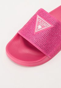 Rosa Riemensandale mit einem strukturierten Riemen, der mit Strass-Akzenten versehen ist, und einem weißen dreieckigen Logo. Weiche Gummisohle mit glatter Oberfläche.