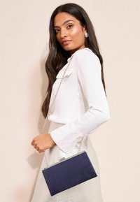 Kabelka z tmavě modré semiše se stříbrným řetízkovým popruhem, obdélníkového tvaru, elegantního designu, hladké textury a kovového zapínání.