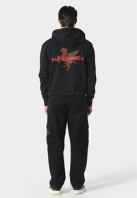 Conjunto de sudadera negra con pantalones cargo. La sudadera presenta un diseño gráfico rojo y texto en la parte posterior. Los pantalones tienen bolsillos laterales y un ajuste casual.