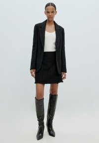 Zwart tweed blazer en rok set met rafelige randen, gecombineerd met kniehoge zwarte leren laarzen, die een getailleerd silhouet en een zachte textuur tentoonstelt.