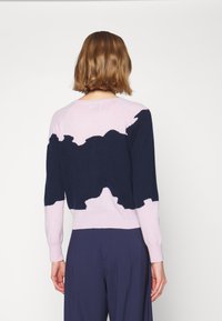 Pull en tricot avec des blocs de couleurs bleu marine et rose clair, encolure arrondie et ourlet côtelé. Texture douce avec un motif contrasté.