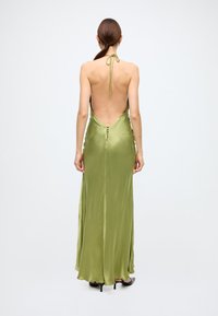 Green satin halter dress with a deep back, featuring button details along the side and a flowing silhouette. Suitable for formal occasions.