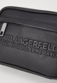 Pochette in pelle nera con texture, caratterizzata da un marchio impresso. Tra le caratteristiche si evidenziano la chiusura con zip e i bordi lisci per un design elegante.