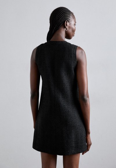 Vestito nero senza maniche realizzato in tessuto texturizzato, con una silhouette aderente e un orlo leggermente svasato, impreziosito da dettagli delle cuciture sul retro.
