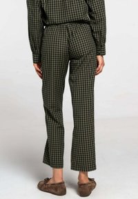 Pantalon à carreaux verts et noirs avec une coupe droite, taille élastique et tissu léger ; porté avec des chaussures marron sans lacets.