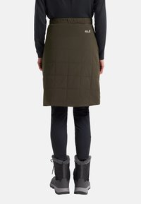 Gequiltede, olijfgroene rok met een elastische tailleband, voorzien van een logo op de achterkant. Gecombineerd met zwarte broeken en winterlaarzen met bontvoering.