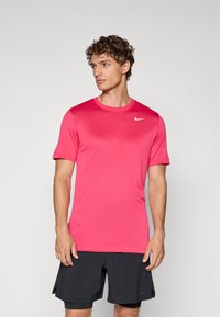 Różowa koszulka sportowa wykonana z gładkiego materiału, z krótkimi rękawami i okrągłym dekoltem, z małym białym logo Nike na lewym ramieniu.